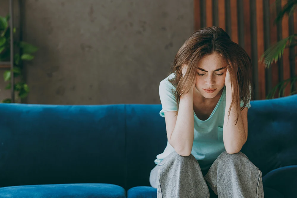 a woman with hands on head sitting on couch
