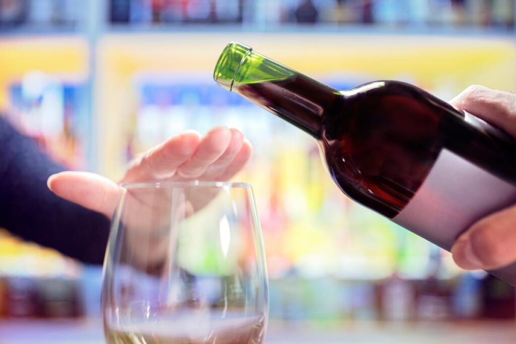 Person putting hand over their glass to reject bottle of wine