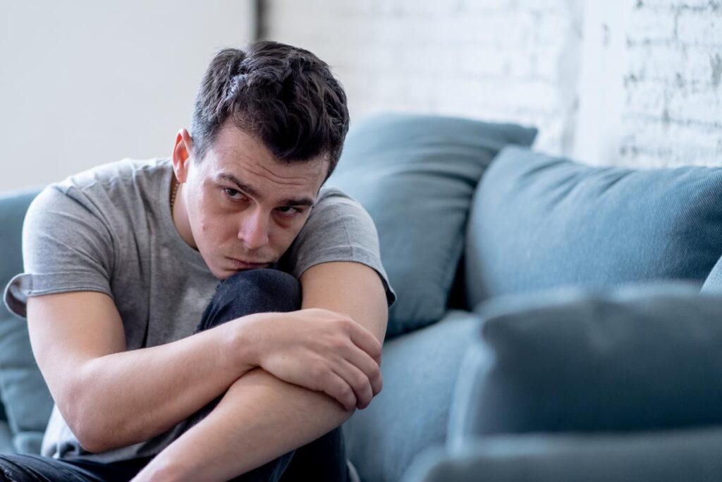 a person sits somberly in front of a couch on the floor possibly struggling with marijuana drug addiction